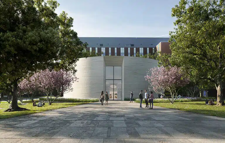 Image showing a modern circular chapel design made of concrete with large glass openings allowing natural light, surrounded by historic buildings in the background.
