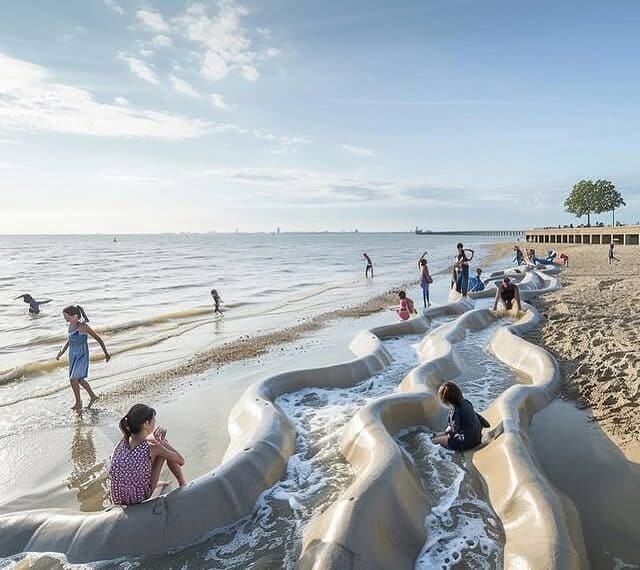 Children playing on coastal architectural sculptures integrated with sand and sea