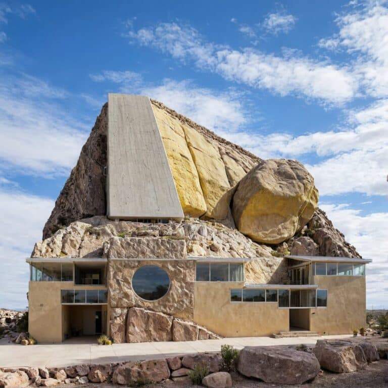 "Rock-integrated home with glass balcony and white concrete facade."