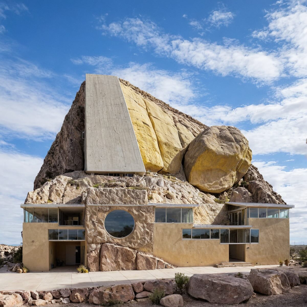 "Rock-integrated home with glass balcony and white concrete facade."