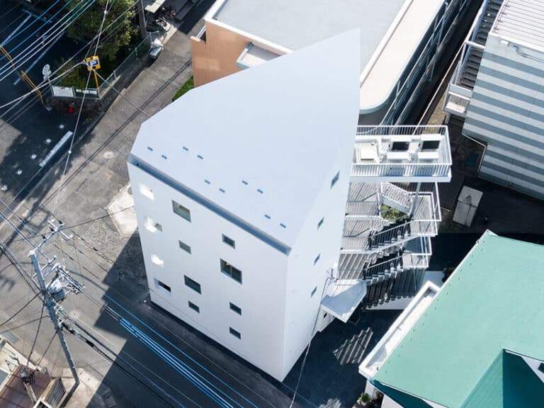 "Aerial view of an innovative residential building showcasing sharp geometric design and asymmetrical windows, with an external staircase leading to upper floors."