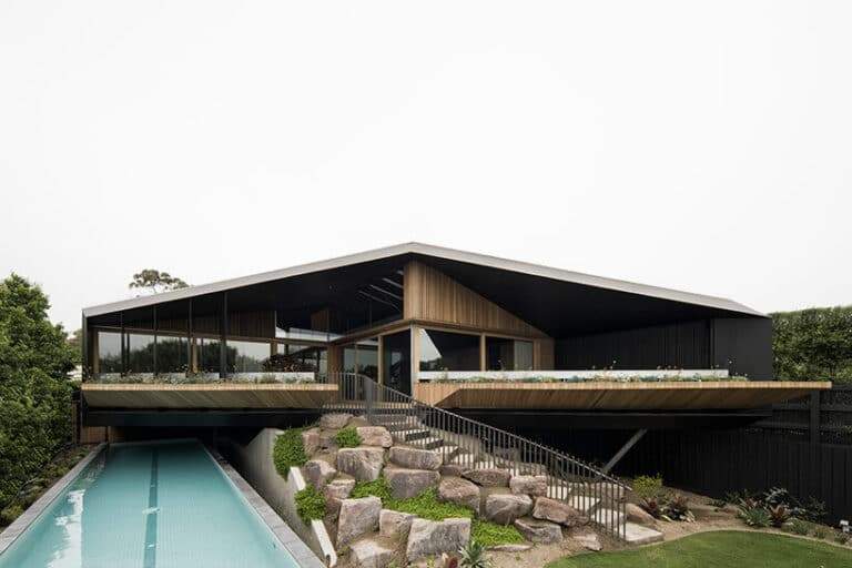 "Exterior view of Kross House floating above natural slopes with sustainable materials like wood and steel."