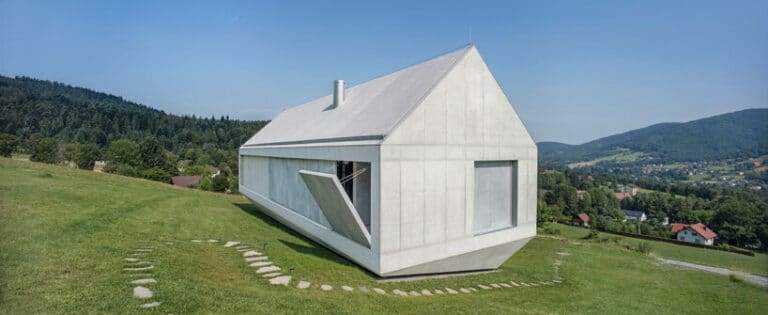 A modern house on a green hillside featuring a movable architectural element on the facade.