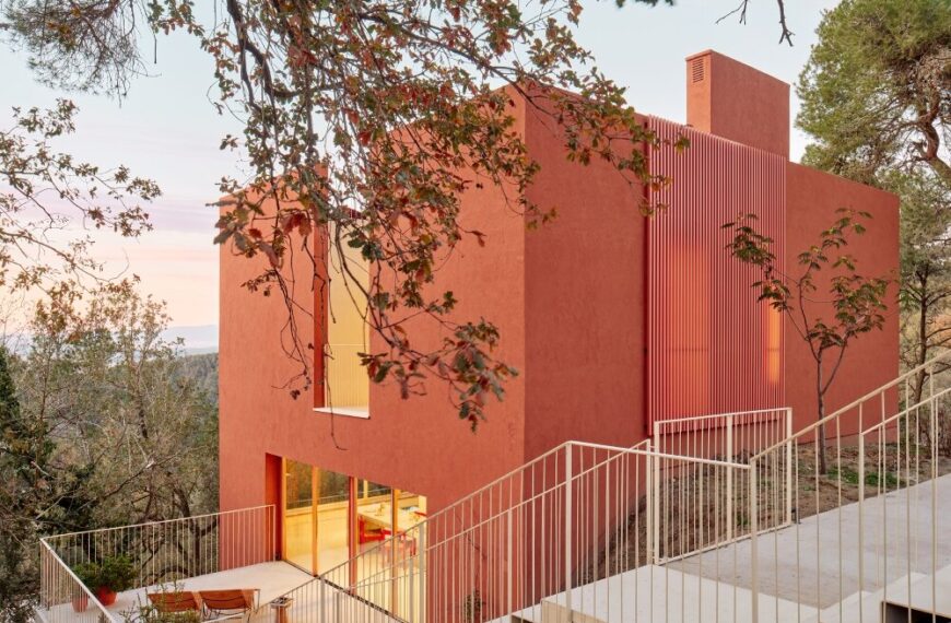 "Modern sustainable house on a steep hillside with natural tones, featuring an outdoor terrace and cantilevered stairs connecting levels."