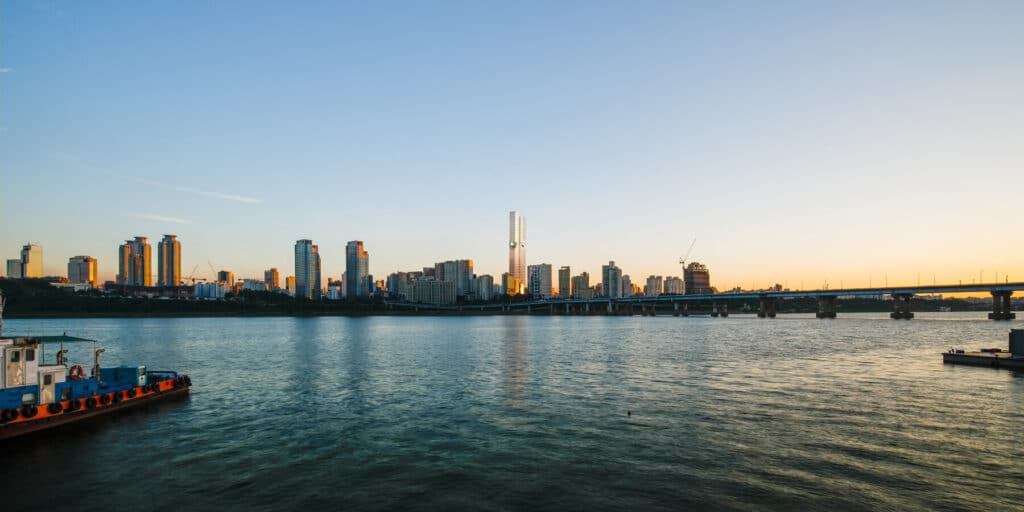 Modern city skyline at sunset with a river and bridge in the foreground