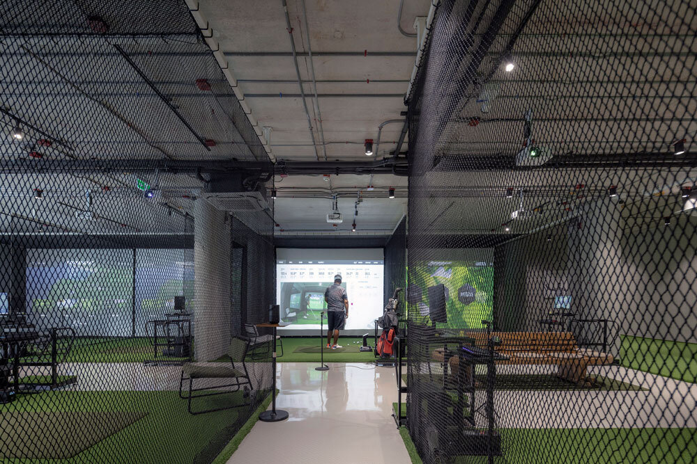 A person using a golf simulator inside an indoor facility with protective netting
