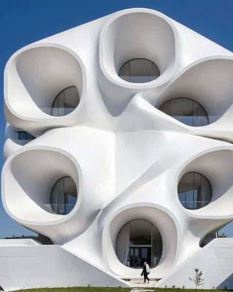 مبنى معماري فريد بواجهة بيضاء منحنية تحتوي على فتحات دائرية، يعكس تصميمه استخدام الذكاء الاصطناعي في الهندسة المعمارية.