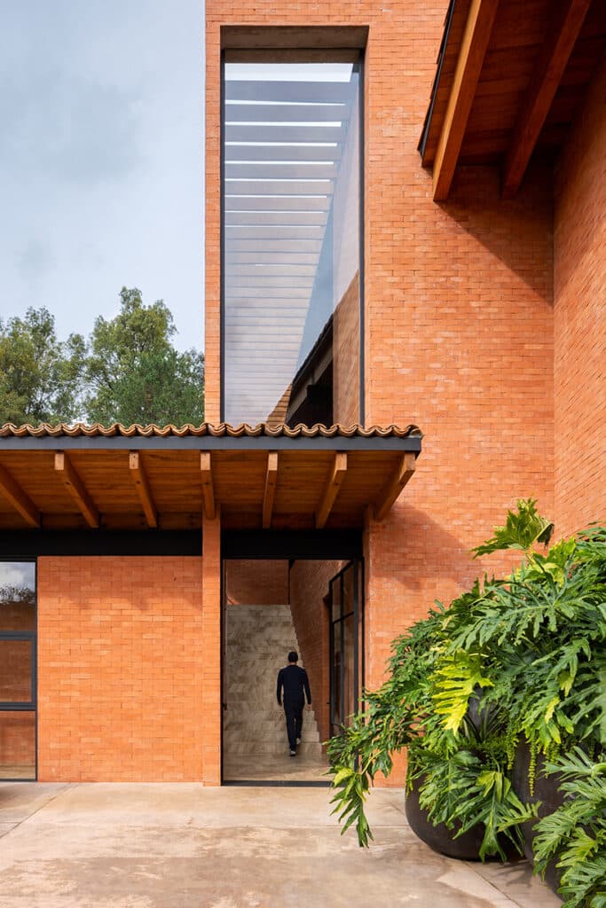 "Modern facade of Hotel Avándaro, showcasing red brick and wood with surrounding greenery."