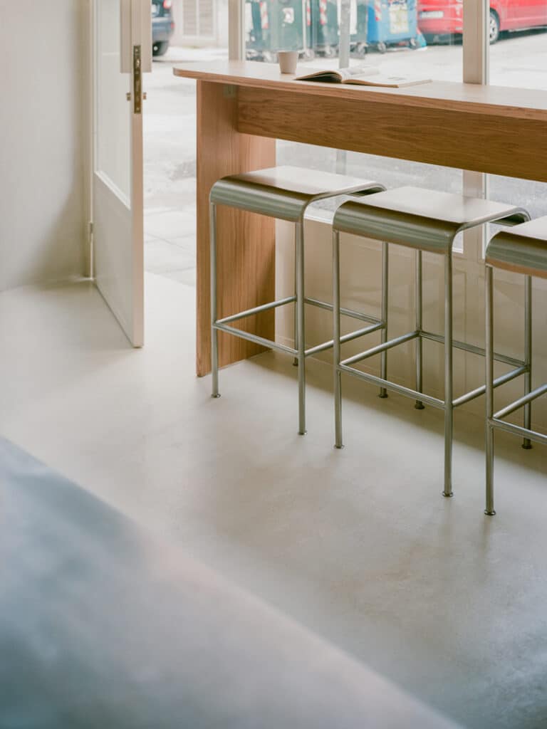 Wooden counter with high metal stools beside a large glass window in a café