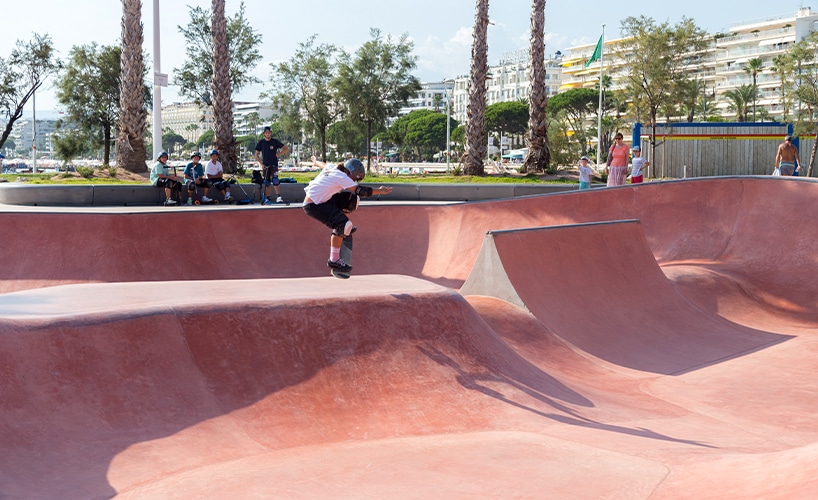 "Skateboarder gliding along the edge of the Cannes skatepark bowl amidst palm trees."