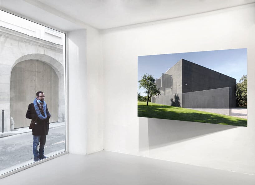 A man stands outside a gallery window looking at a photograph of a modern concrete building displayed inside.