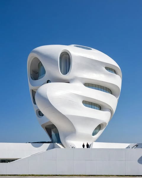 مبنى معماري مستقبلي بواجهة بيضاء منحنية تحتوي على فتحات دائرية، يعكس تصميمه استخدام الذكاء الاصطناعي في الهندسة المعمارية.