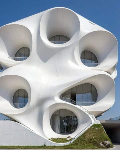 مبنى معماري فريد بواجهة بيضاء منحنية تحتوي على فتحات دائرية، يعكس تصميمه استخدام الذكاء الاصطناعي في الهندسة المعمارية.