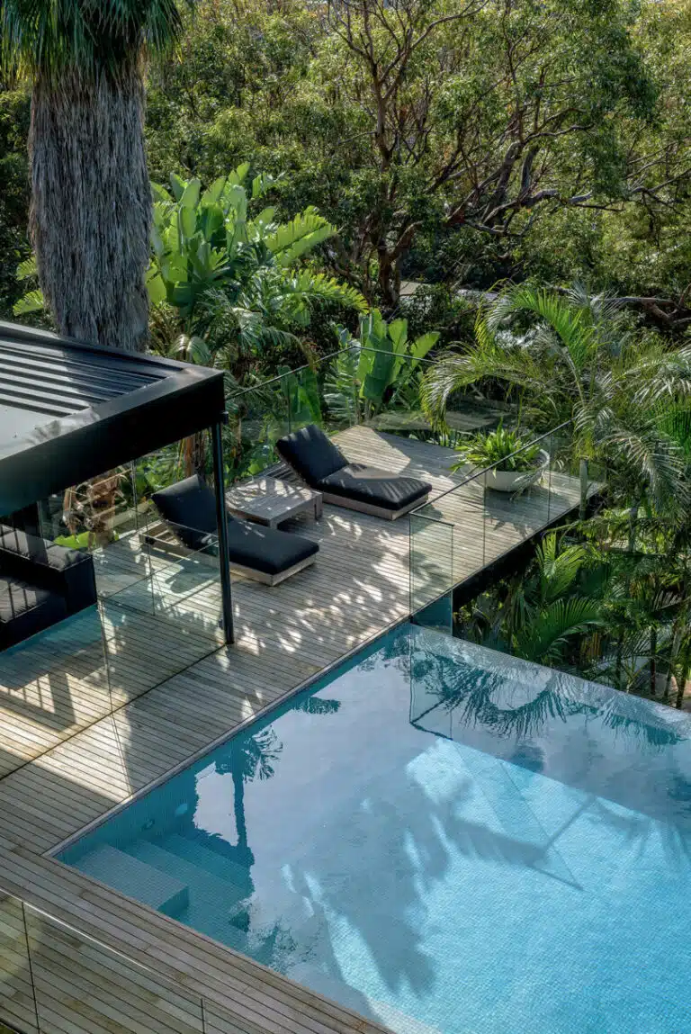 Experience the epitome of LA Cool at our rooftop infinity pool, elegantly framed with glass railing and lush greenery. Relax on two cushioned lounge chairs under a sleek black pergola, perfectly poised on a stylish wooden deck.