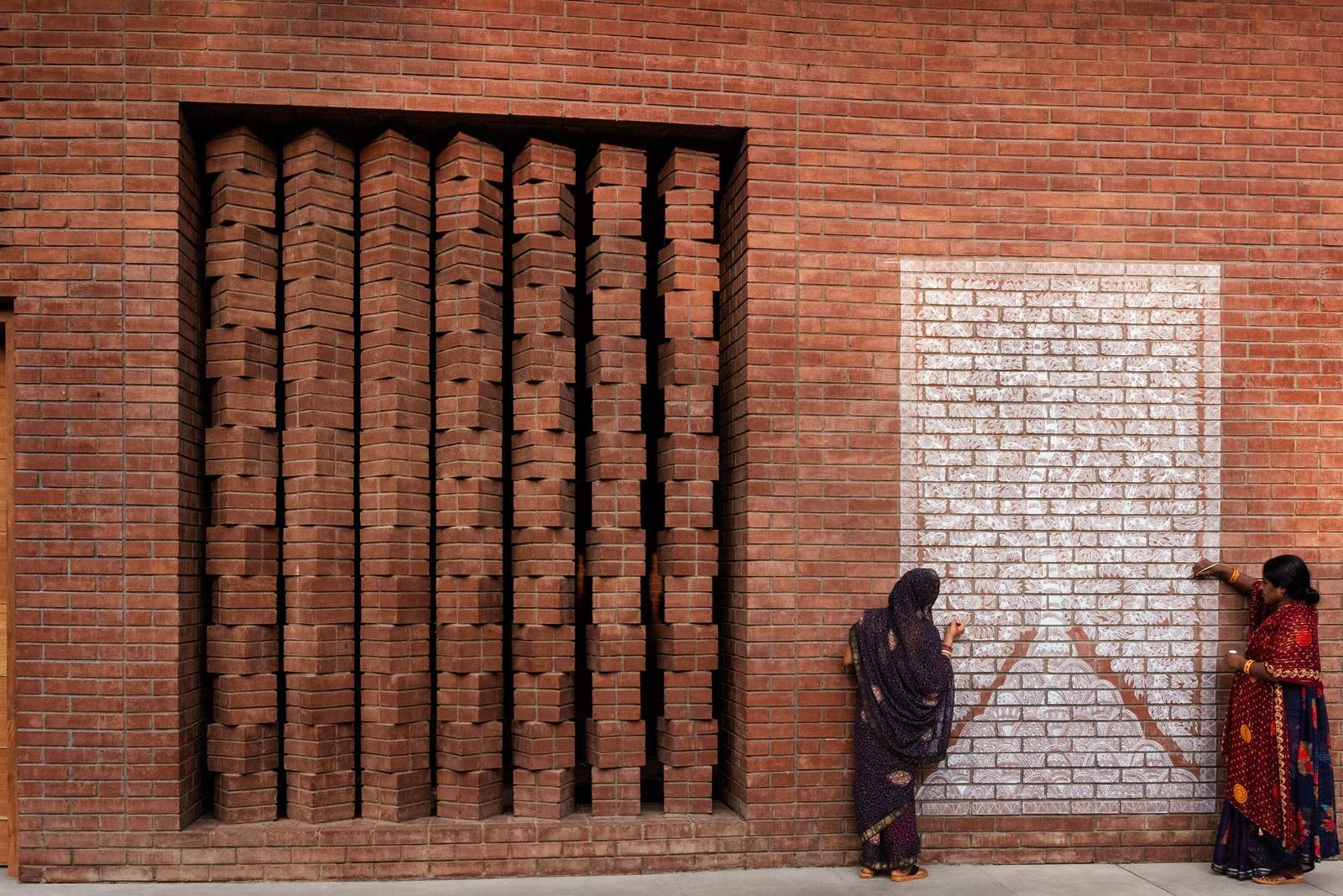 Two women in saris creating a mural on a brick wall