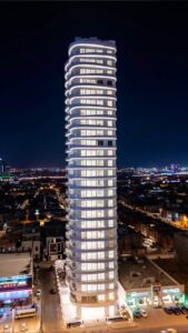 At night, The Oval Residential Tower is illuminated, highlighting its elegant curves and glassy exterior, creating a striking silhouette against the city lights of Riyadh.