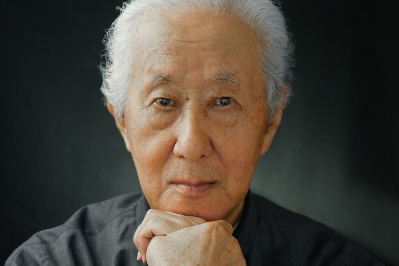 A portrait of renowned architect Arata Isozaki, standing confidently in front of a modern building.
