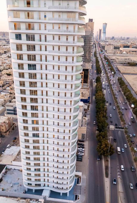 A modern, curvilinear residential tower stands tall on King Fahd Road in Riyadh, showcasing its sleek design against the backdrop of a bustling urban landscape.