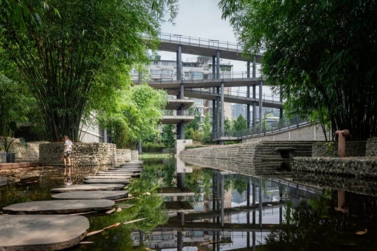"An architectural design by Liu Jiakun that blends nature and urban life, featuring a wooden walkway over a small waterway and modern buildings."