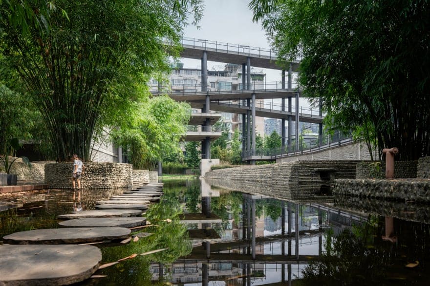 "An architectural design by Liu Jiakun that blends nature and urban life, featuring a wooden walkway over a small waterway and modern buildings."