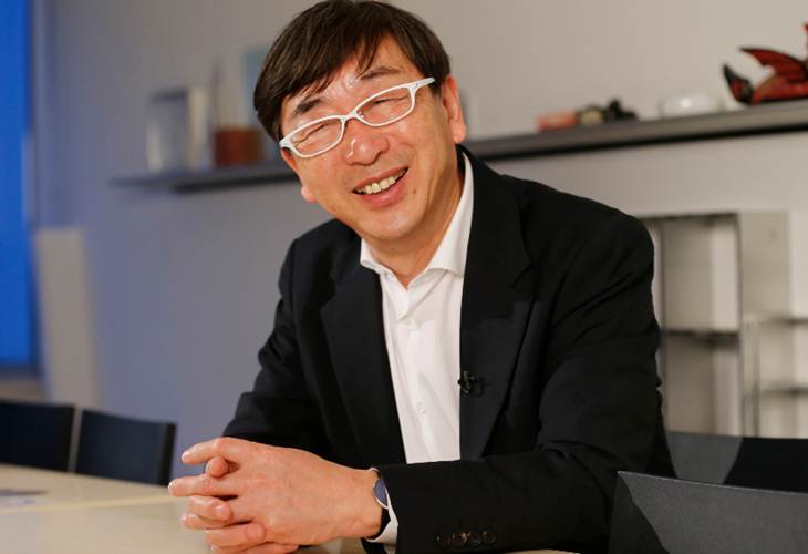 "Toyo Ito, the renowned Japanese architect, smiling in a modern office setting, reflecting his innovative and unique approach to architecture."