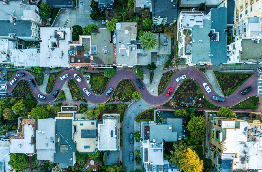 Aerial image of a curvy, bustling urban road lined with residential buildings and green spaces, highlighting the harmony between urban planning and the environment.