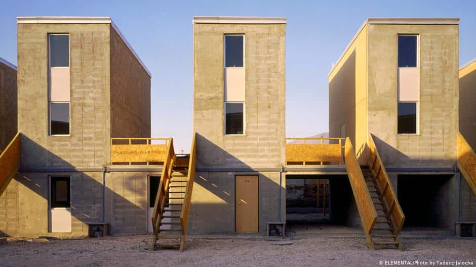Three simple brick homes with wooden outdoor stairs, standing under a clear sky, showcasing the concept of half-finished housing.