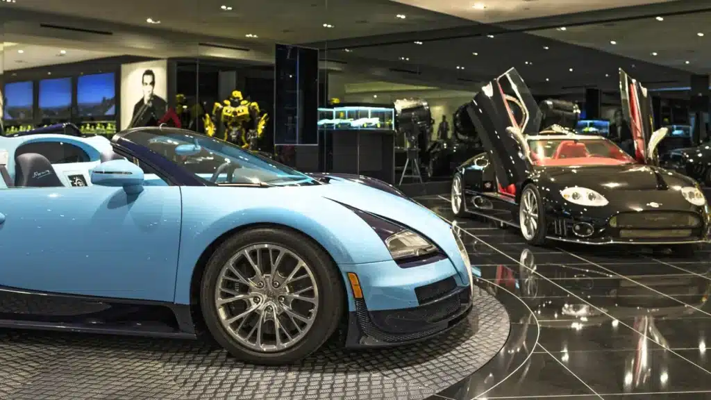 "The car display garage of the Beverly Hills mansion, showcasing luxury cars like Bugatti and a Bumblebee robot sculpture."