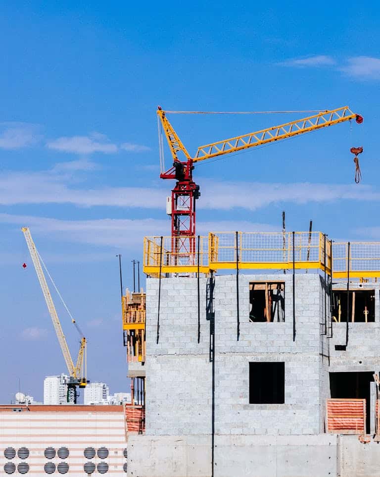A photo of a building under construction with a tall yellow crane lifting heavy materials against a clear blue sky.