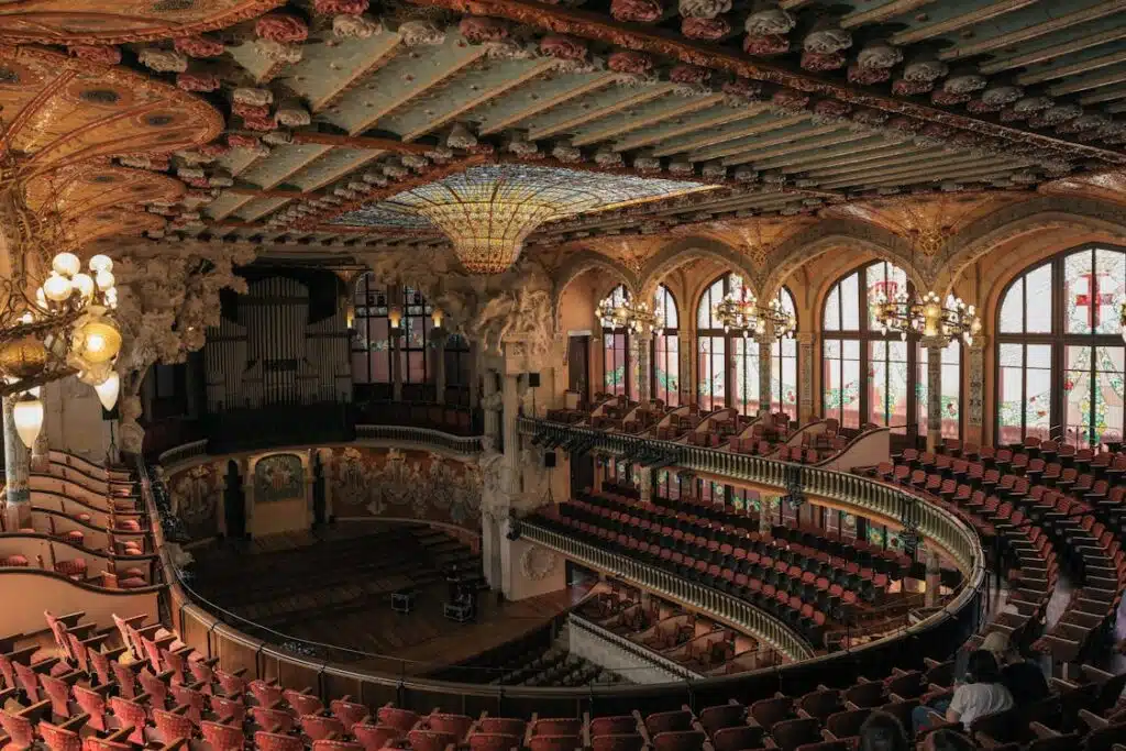 An opulent theater hall with a traditional design, featuring an ornate ceiling and colorful stained glass windows, with meticulously arranged seats to ensure optimal sound distribution for the audience