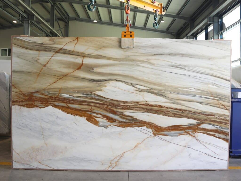 : White marble slab with golden patterns being lifted during marble manufacturing in the factory