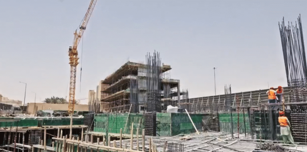 موقع بناء قيد الإنشاء يظهر فيه برج تحت التطور مع برج كرين ضخم في الخلفية، وعمال يرتدون ملابس أمان يقومون بأعمال البنا