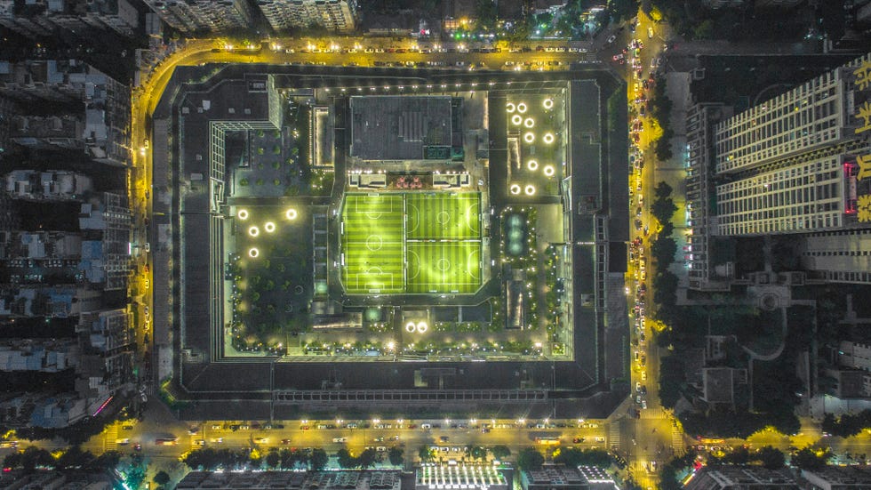 "An urban architectural design by Liu Jiakun featuring a central green space illuminated at night, blending nature with the city."