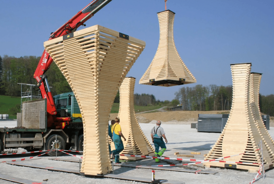 Workers overseeing the lifting of large wooden pieces using a crane, as part of a construction project featuring innovative engineering designs