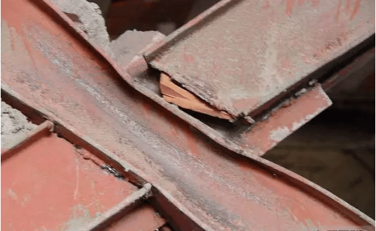A close-up view of a red-painted metallic structure with concrete attached to it, showcasing the integration of metal and concrete in a robust construction process.