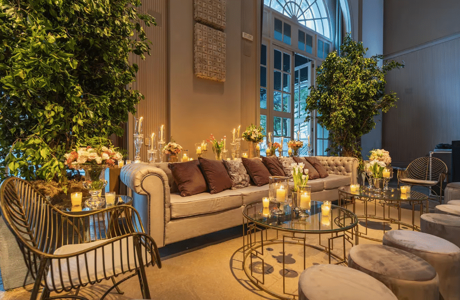 A luxurious living room with a white sofa and modern furniture, illuminated by candles and surrounded by green plants and colorful flowers, creating a warm and cozy atmosphere.