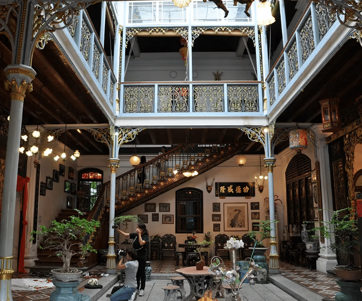 A traditional indoor courtyard featuring elegant architectural design and intricate ornamentation, with plants and tables adding a sense of comfort and beauty.
