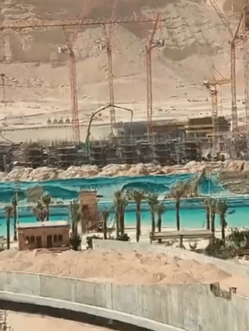 Construction progress at Aquaria Park in Qiddiya City, showcasing expansive water areas surrounded by palm trees.
