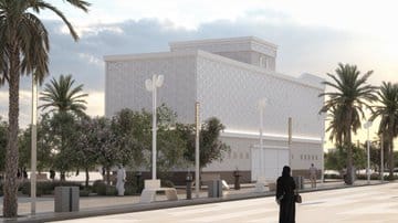 A photo of a brand-new modern building with a smooth white facade covered in subtle geometric patterns. The structure sits in the middle of a green area surrounded by tall palm trees, giving off that