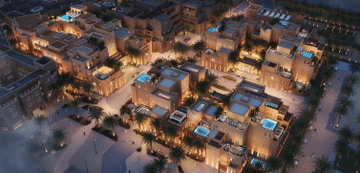 Aerial view of the Armani Residences project in Diriyah at night, showing traditional stone buildings with illuminated infinity pools and surrounding palm trees enhancing the scenery.
