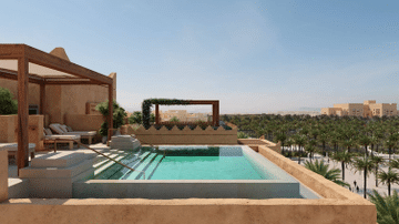 صورة لشرفة في أرماني ريزيدنس الدرعية تطل على مسبح لا متناهي مع إطلالة على غابات النخيل ومباني تقليدية تحت سماء صافية.