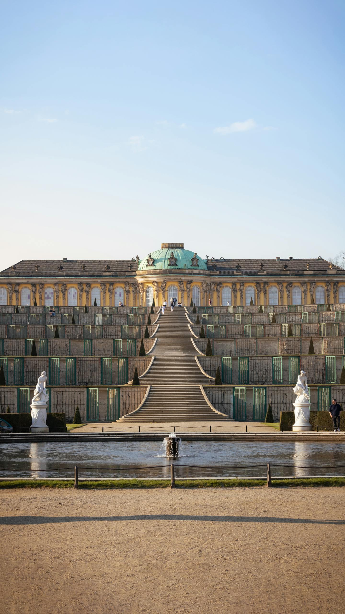 A breathtaking view of Sanssouci Palace's grand staircase and fountain under a clear blue sky.