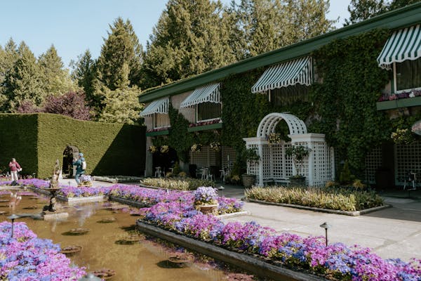 A beautifully landscaped garden with colorful flowering plants and green trees in the background, featuring a building with a shaded balcony