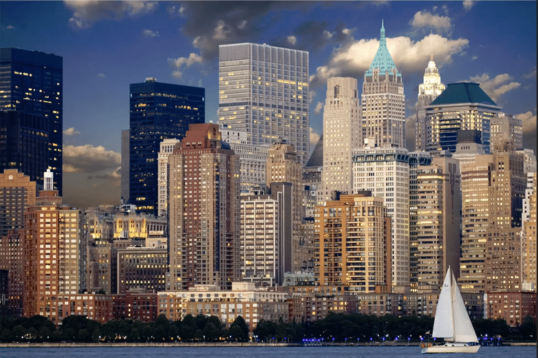 A vibrant view of New York City at night, where towering skyscrapers and modern buildings illuminate the waterfront, with a sailboat peacefully cruising in the water.