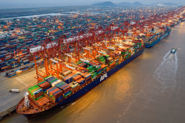 A bustling port filled with containers, featuring a large cargo ship loaded with freight, surrounded by massive cranes under the glow of sunset.