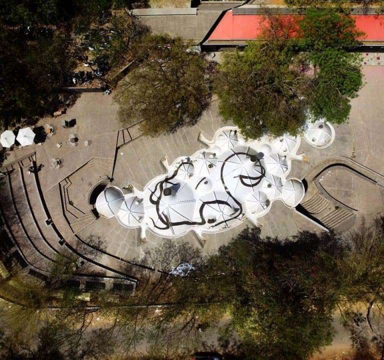 Aerial view of a modern architectural design featuring an open space with white umbrellas surrounded by trees.