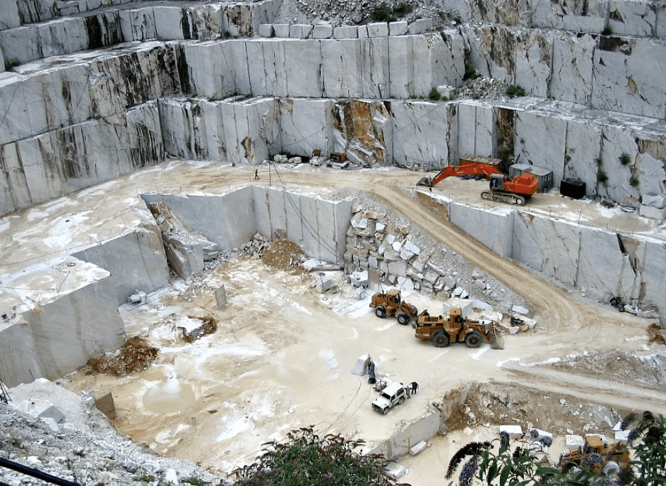 "Wide view of a natural marble quarry showing large blocks of white marble with heavy machinery used in the extraction process."