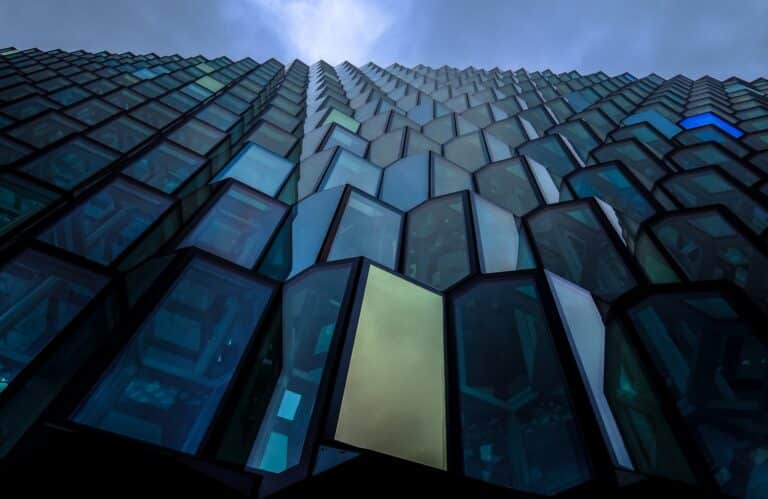 واجهة مبنى ناطحة سحاب تحتوي على تصميم زجاجي هندسي فريد، يُظهر تأثيرات الضوء والظل بشكل درامي