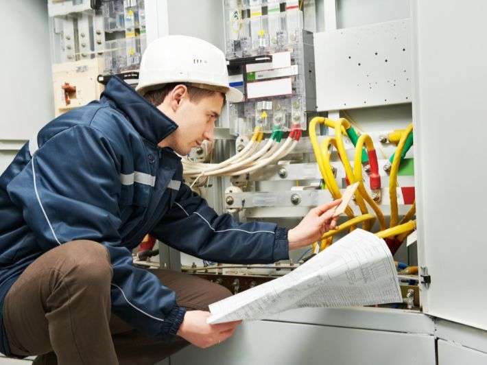 "مهندس كهربائي يراجع الخرائط الفنية أثناء العمل على لوحة التحكم الكهربائية