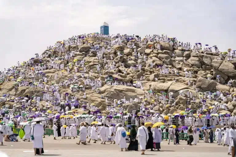 Crowds of pilgrims in white garments holding colorful umbrellas as they gather on Mount Arafat.